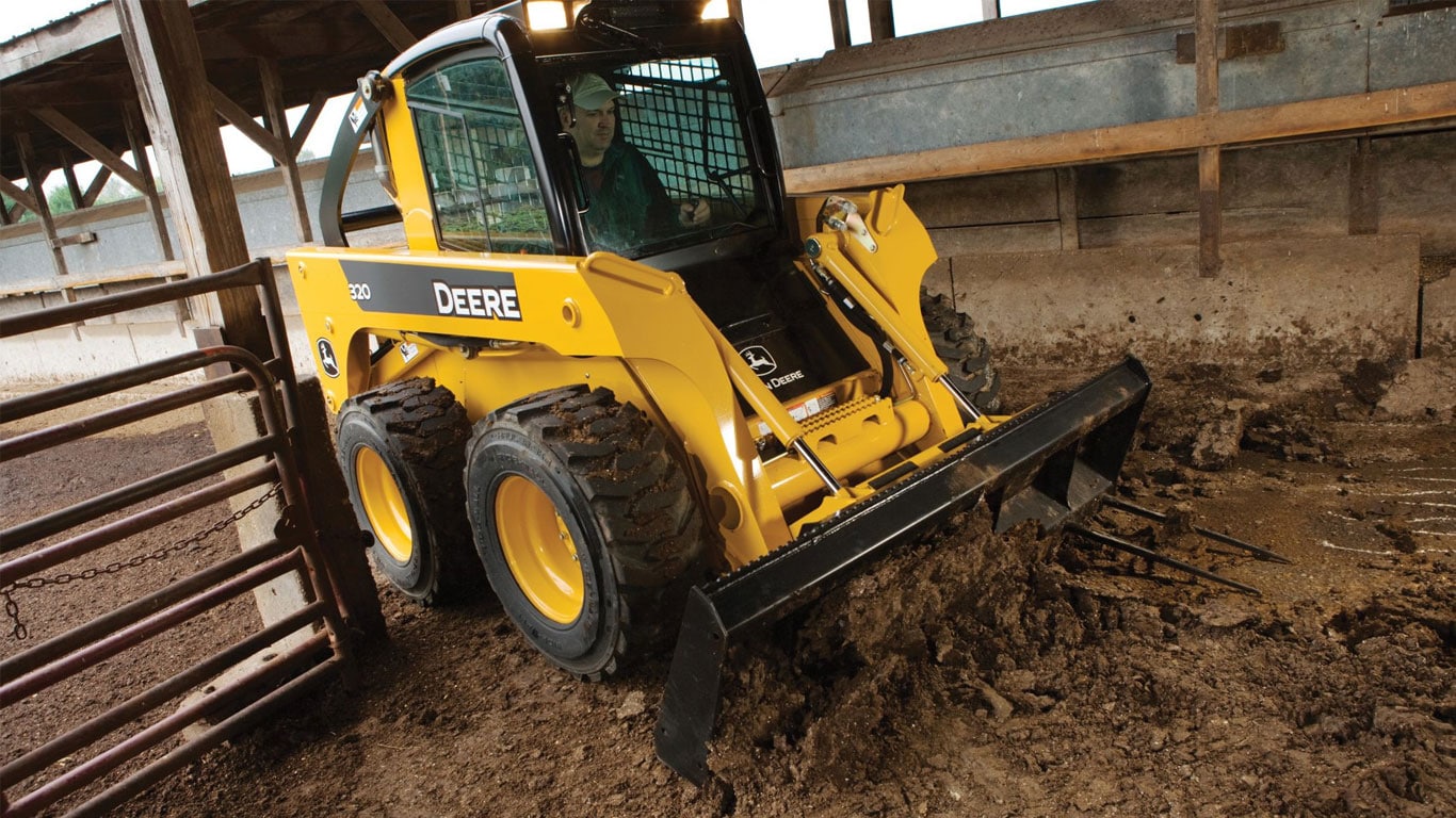 John Deere skid steer with root rake attachment working on farm.